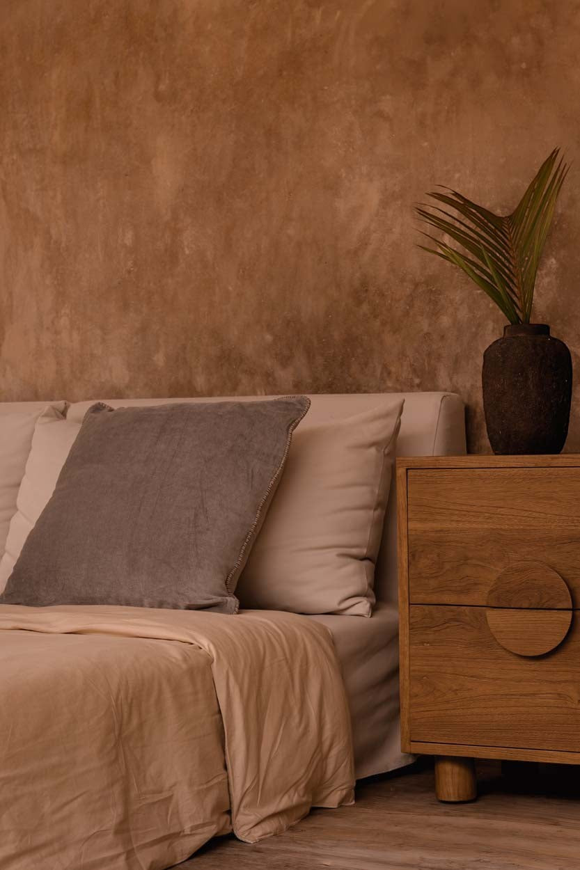 Kayu Living Eclipse solid teak nightstand with two drawers and circular handle in a warm, modern bedroom setting.