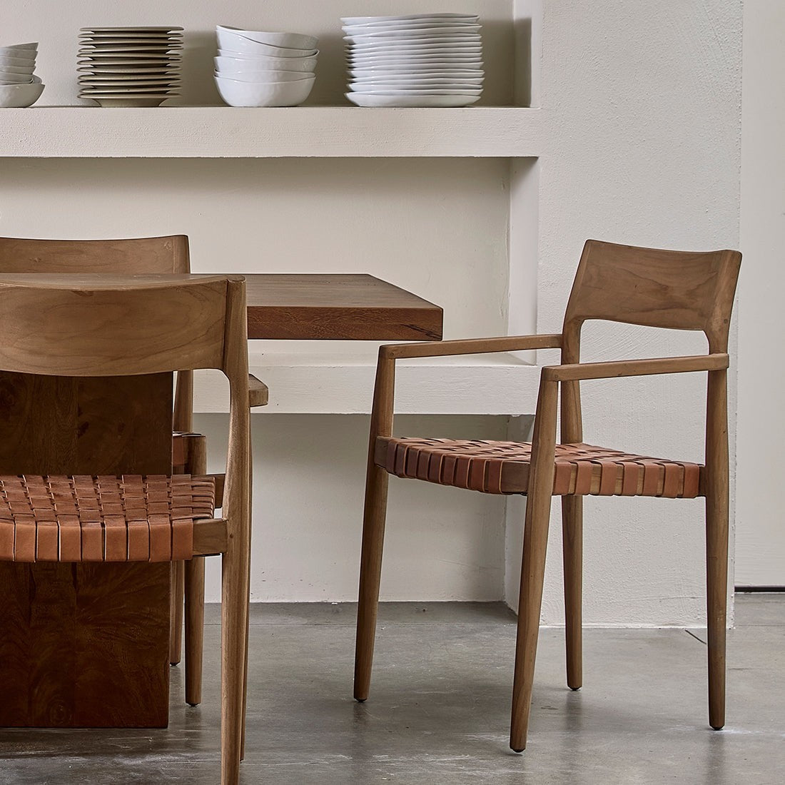 Kayu Living Freya teak dining chairs with brown woven leather seats and armrests in a minimalist dining room.