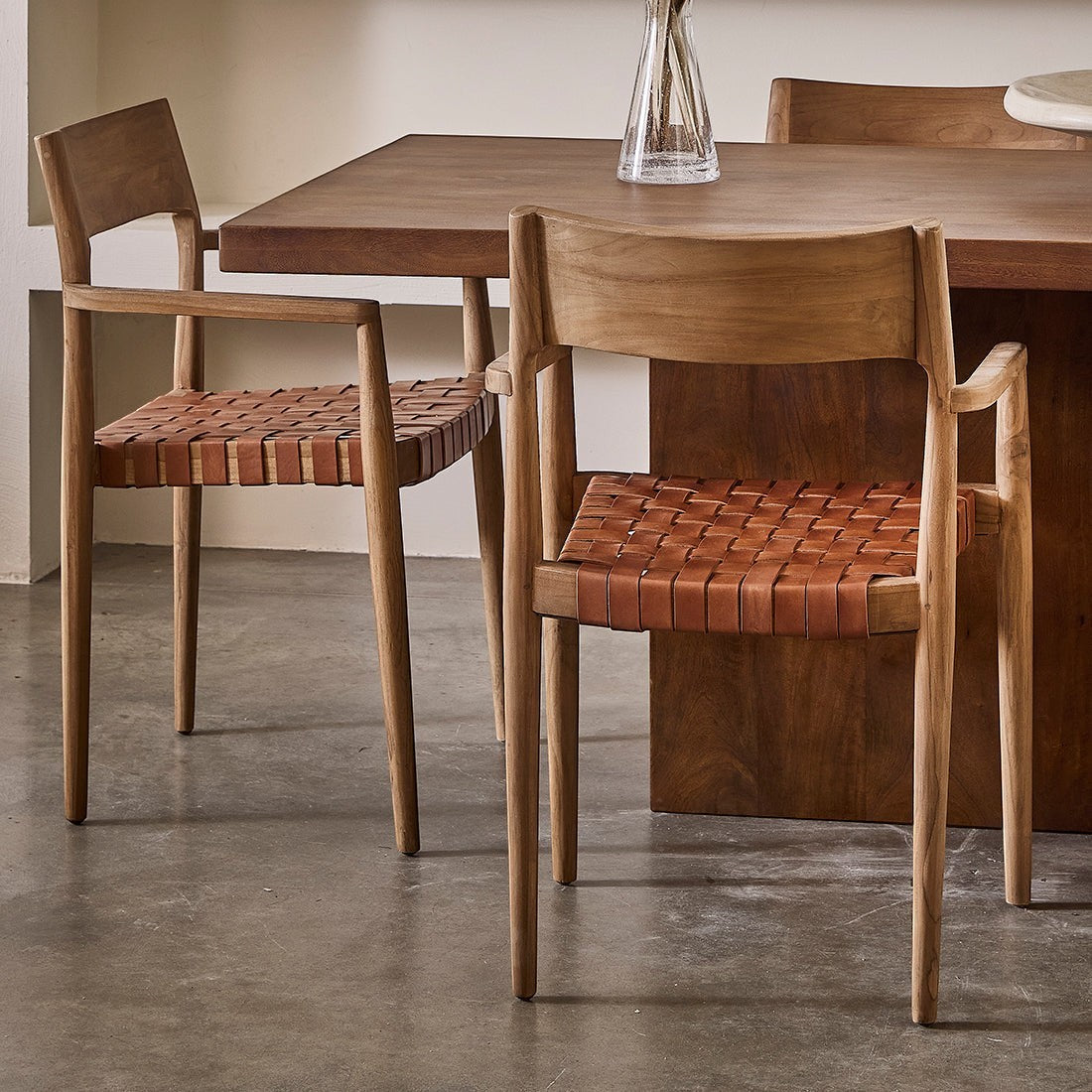 Kayu Living Freya brown teak dining chair set with armrests and woven leather seat in a modern dining room setting.