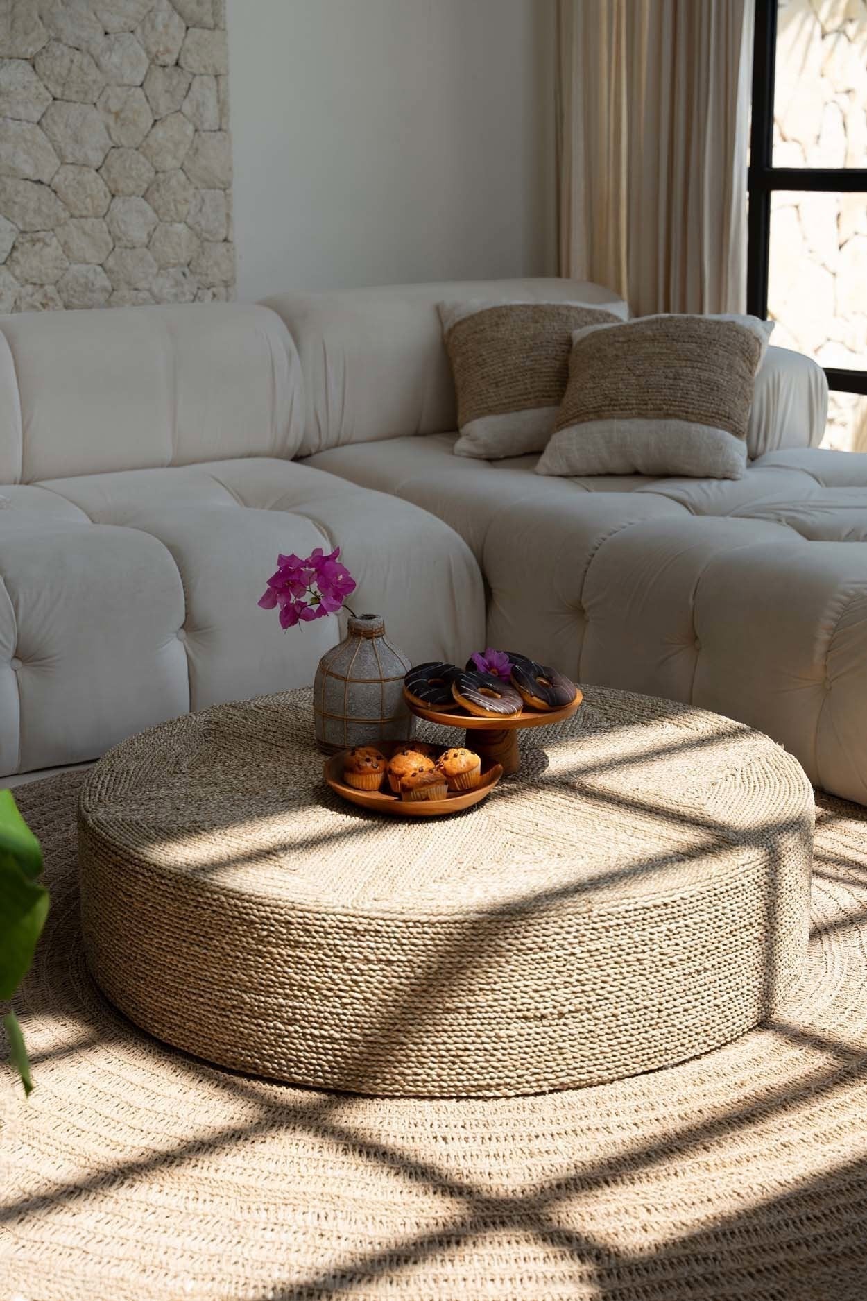 Kayu Living large round seagrass pouf used as a coffee table in a bright living room with a white sofa