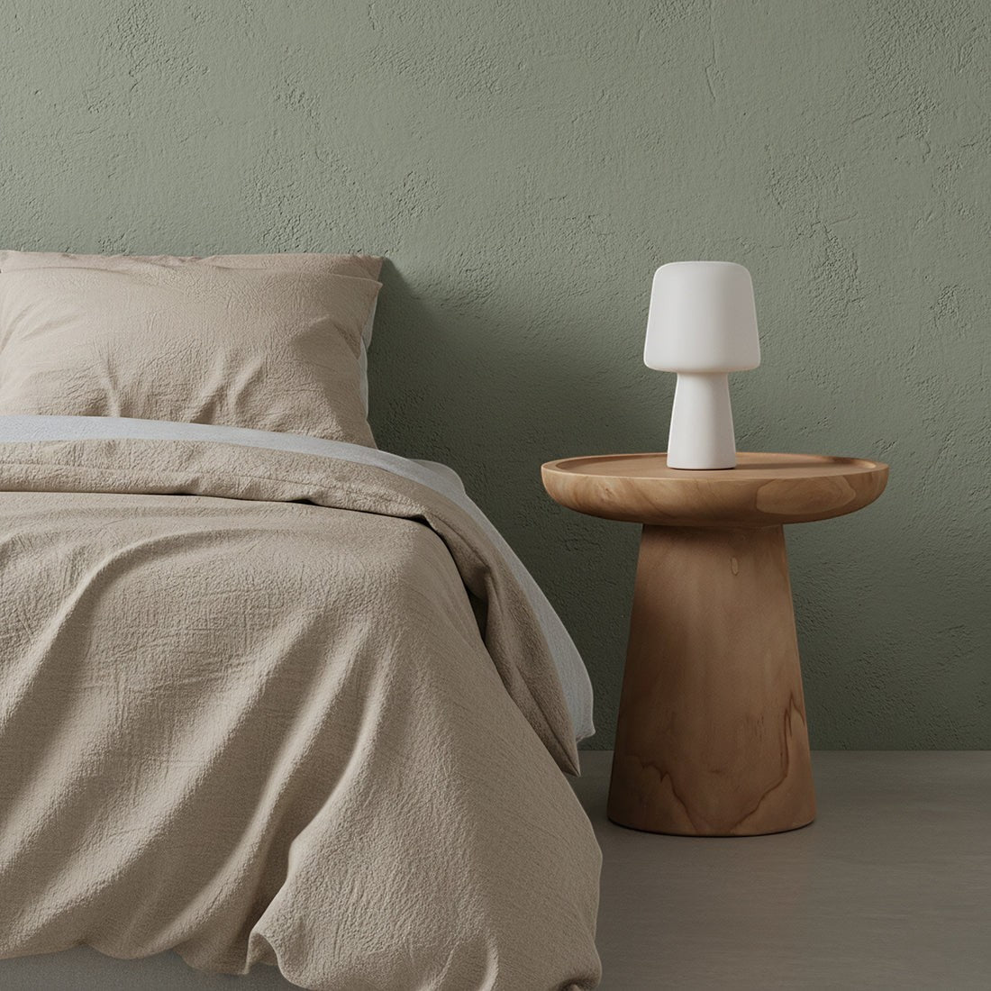 Kayu Living Nero Ray teak side table with a minimalist round top and pedestal base next to a bed in a bedroom.