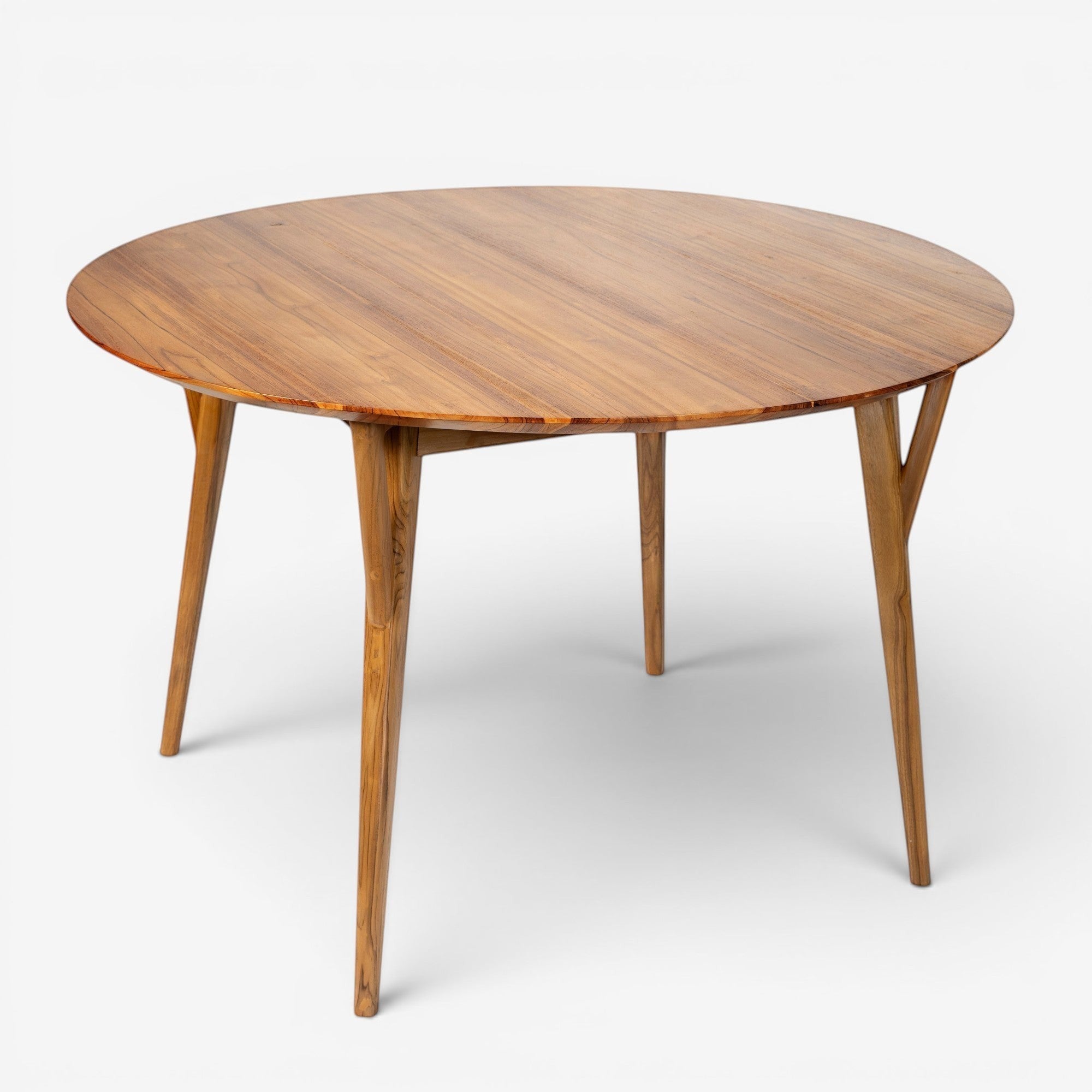 Kayu Living Pantai round 120 cm teak dining table with natural wood grain and tapered legs.