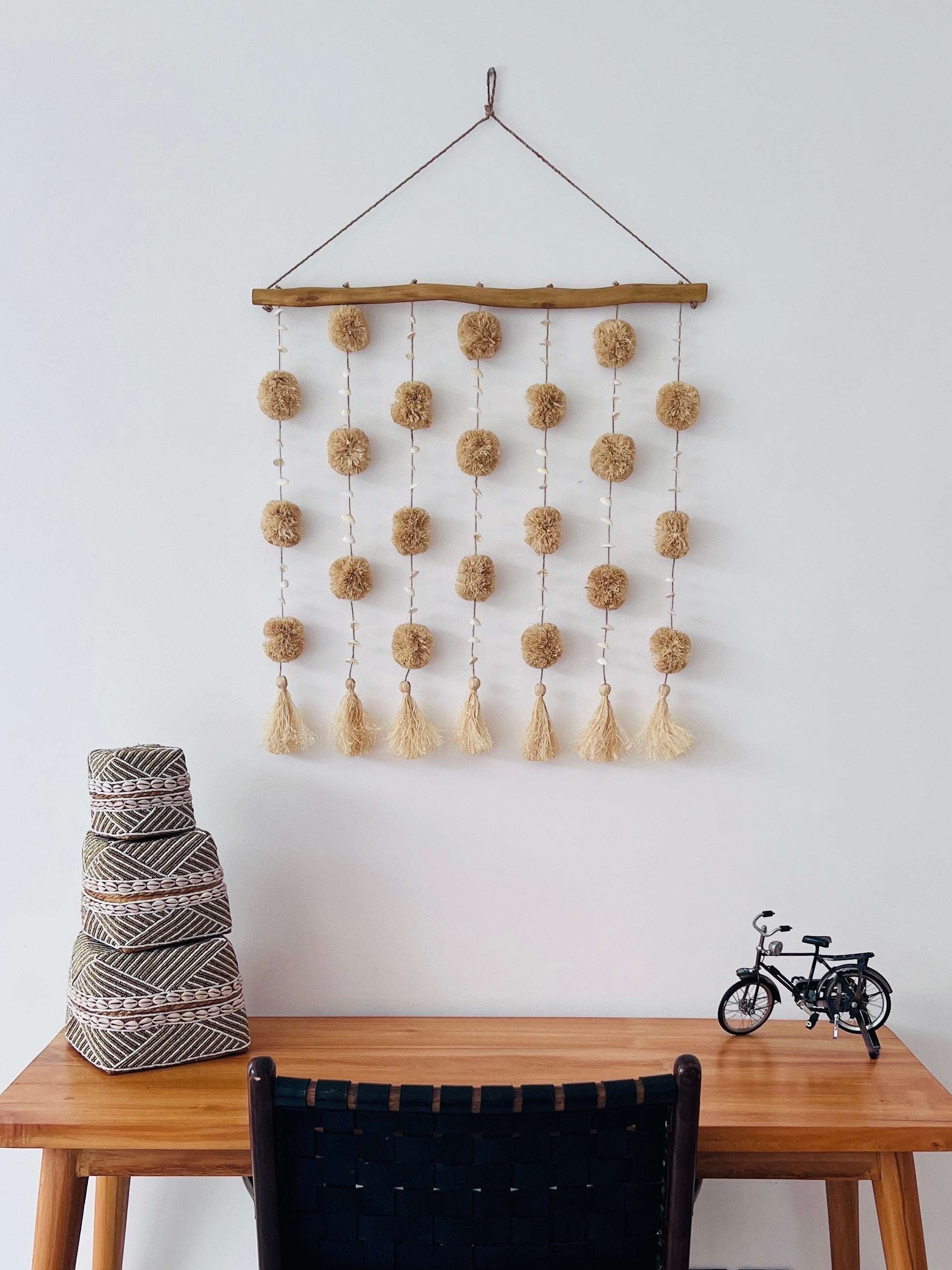 Kayu Living natural beige pom pom wall hanging with tassels and shells on driftwood.