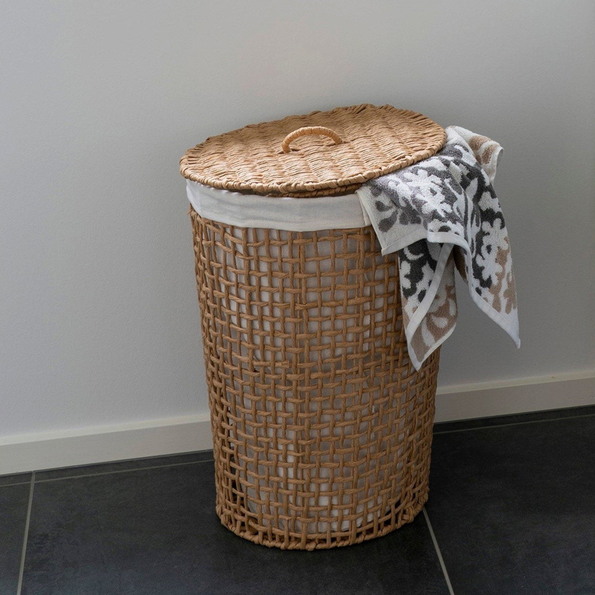 Kayu Living Pomal laundry basket in natural paper with a white liner and lid, placed in a bright room.