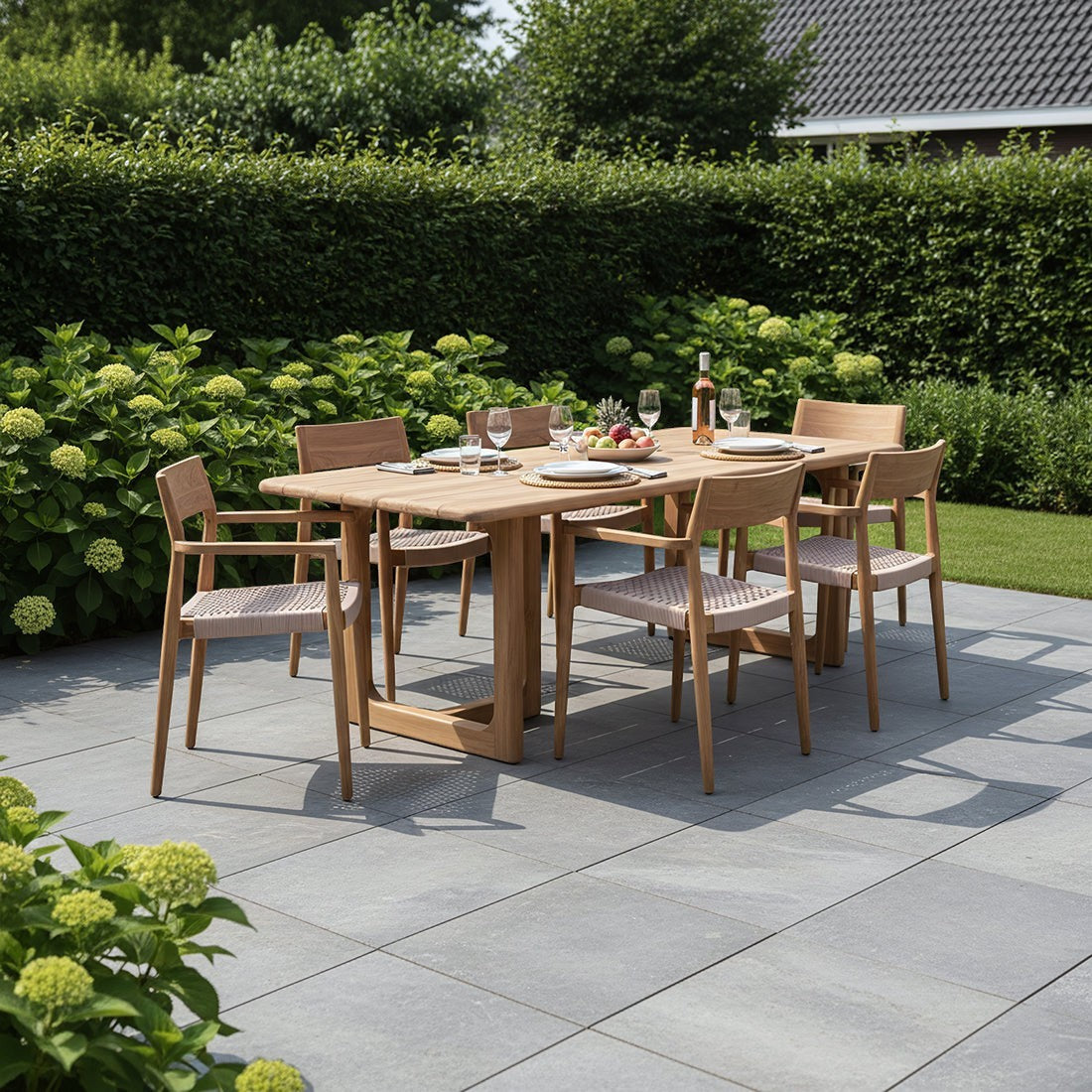 Kayu Living Primavera 240cm teak garden table with matching chairs on a stone patio in a lush green garden setting.
