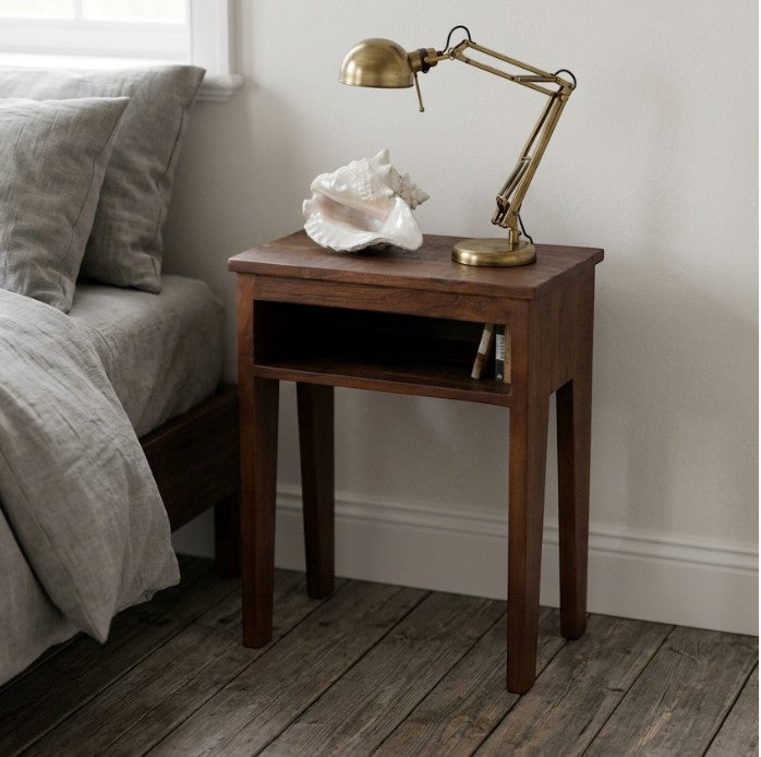 Kayu Living Factory bedside table in dark FSC-recycled wood with an open shelf and tapered legs in a cozy bedroom.