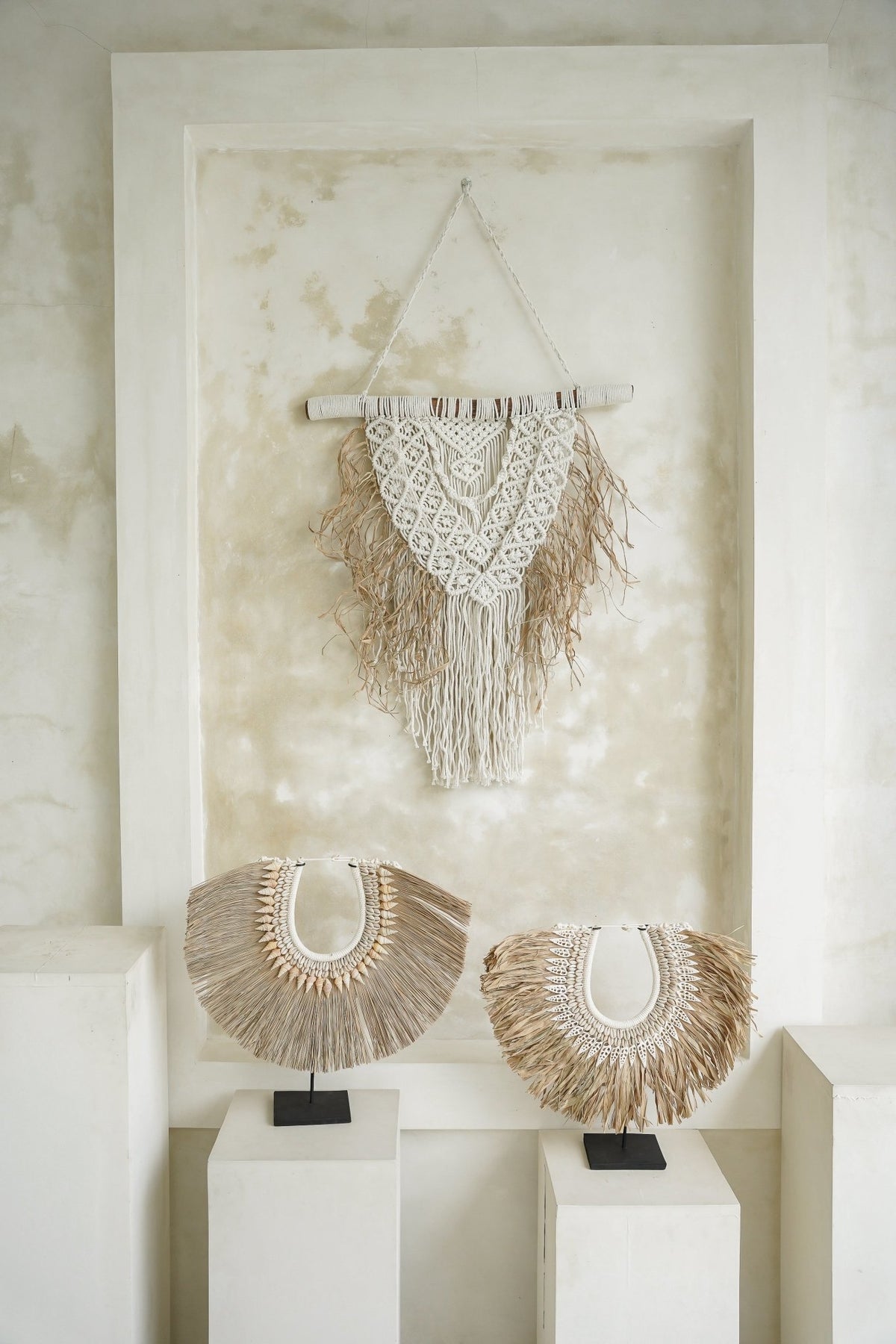 Kayu Living handcrafted seagrass and shell wall hanging and two tabletop shell ornaments on stands in a neutral room.