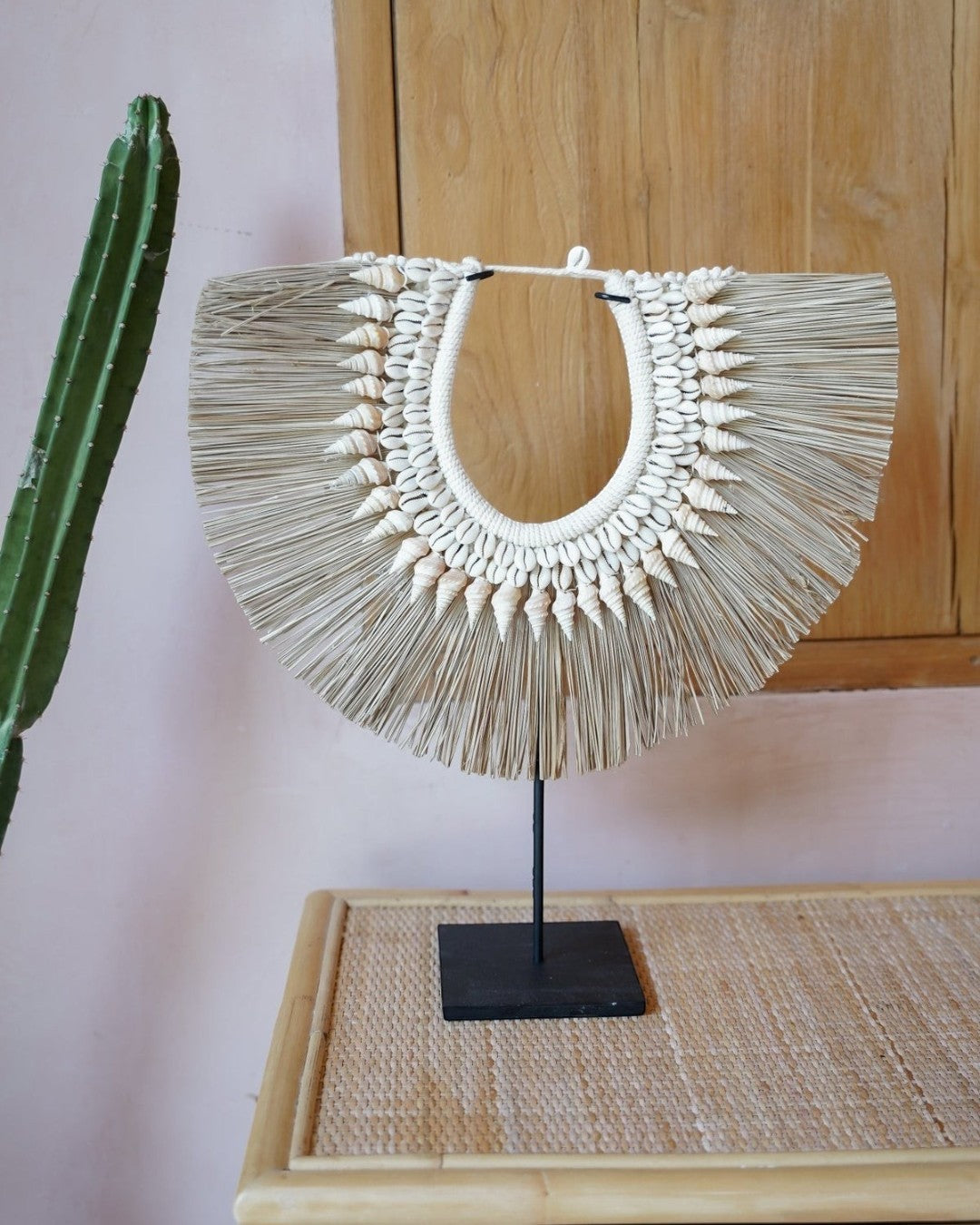 Kayu Living handmade seagrass and shell wall hanger on a black metal stand, featuring natural neutral tones.