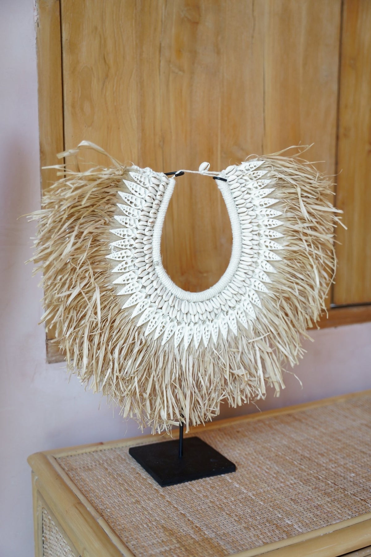 Kayu Living handcrafted seagrass and white shell wall hanging on a black metal stand with organic coastal design.