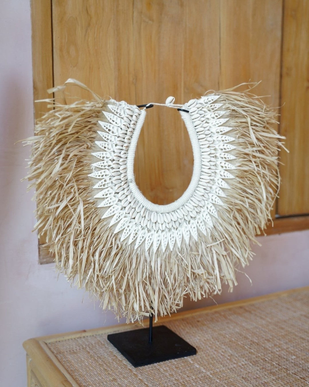 Kayu Living handcrafted seagrass and seashell necklace ornament on a black metal display stand for coastal decor.