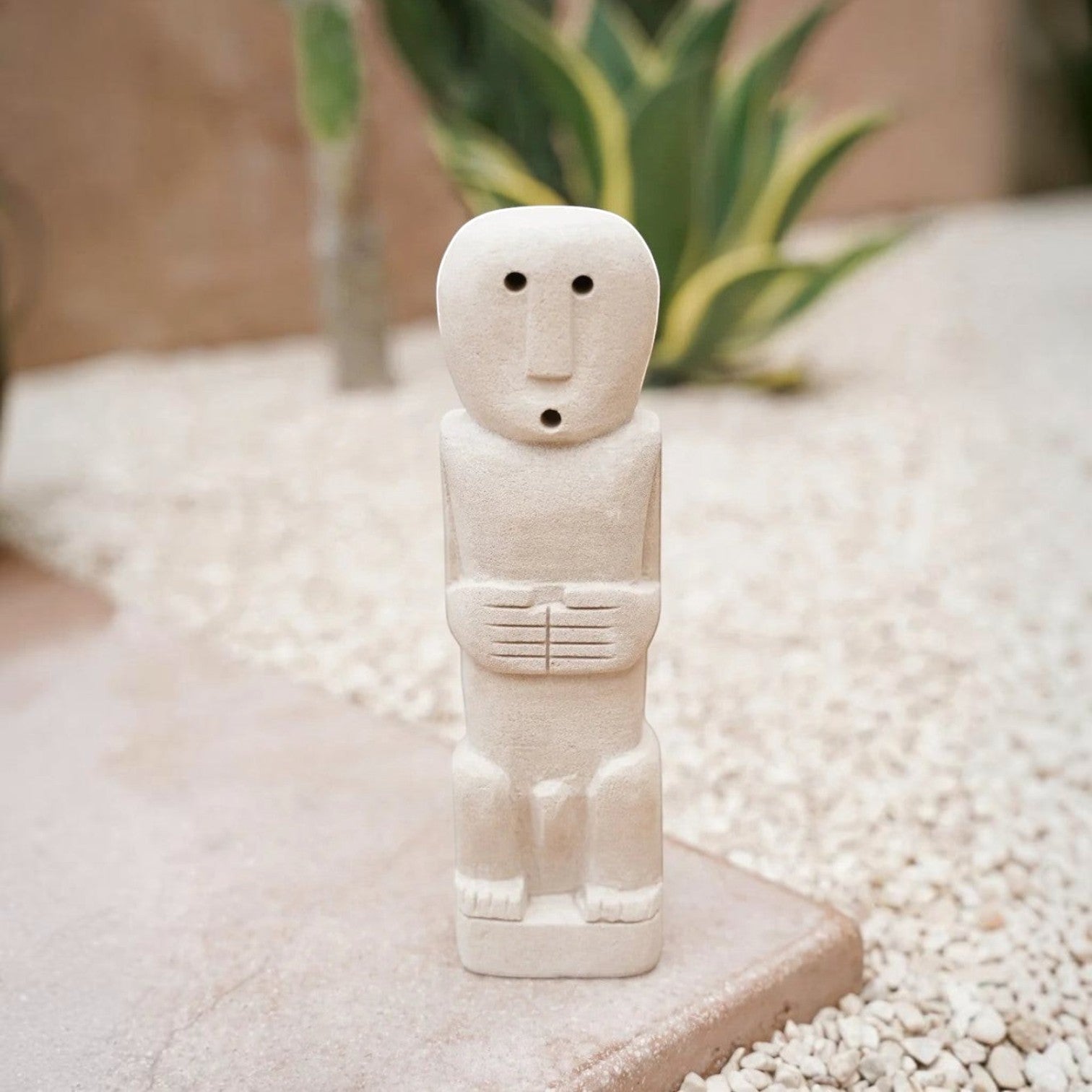 Kayu Living handmade stone gatekeeper figurine with a minimalist carved face and hands, standing on a stone surface.