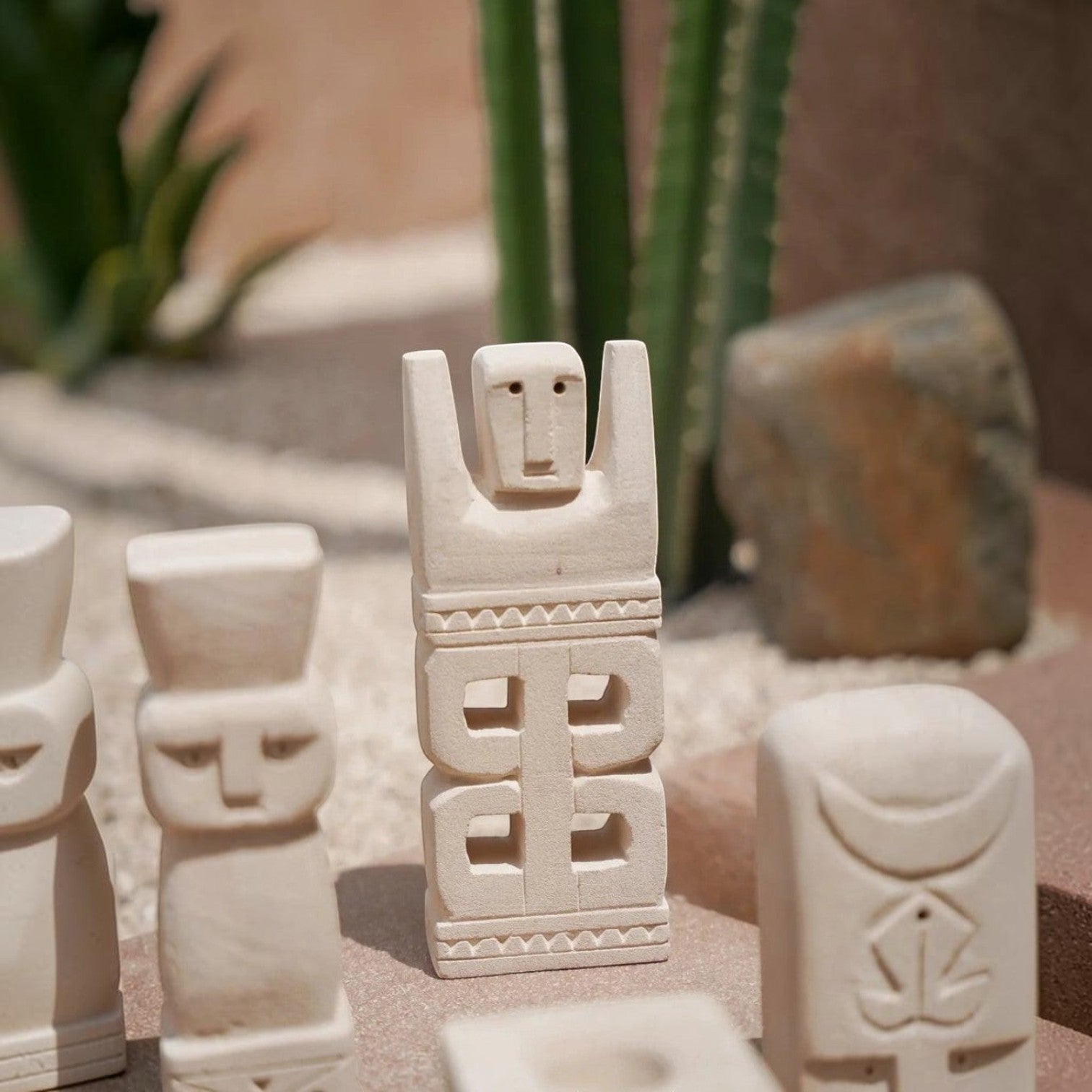 Kayu Living hand-carved stone guardian figurine with natural finish and geometric patterns in a desert setting.