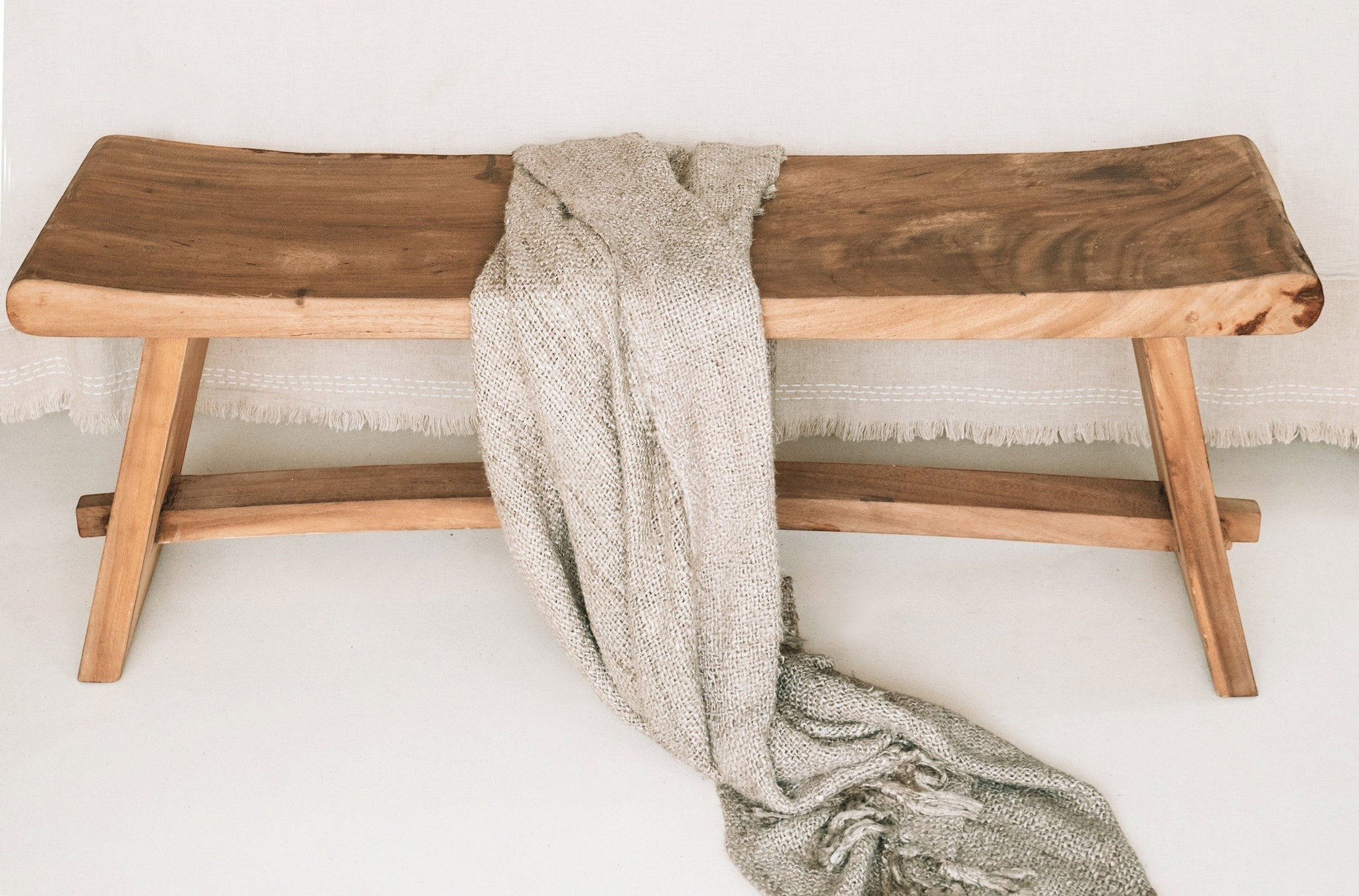Kayu Living 120 cm handmade solid Suar wood bench with natural grain and a draped beige textured throw blanket.