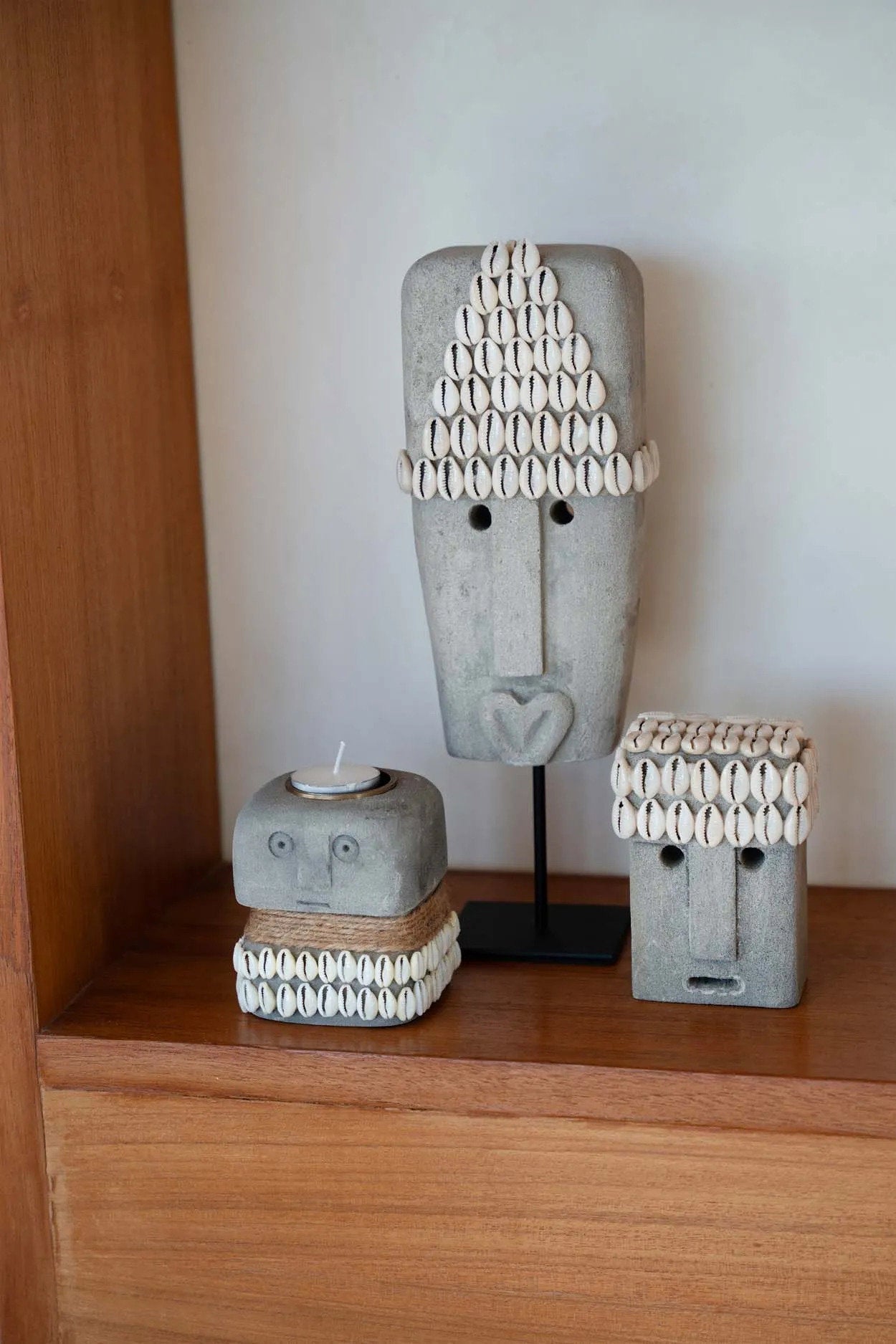 Kayu Living hand-carved grey sandstone Sumba statues decorated with cowrie shells on a wooden shelf