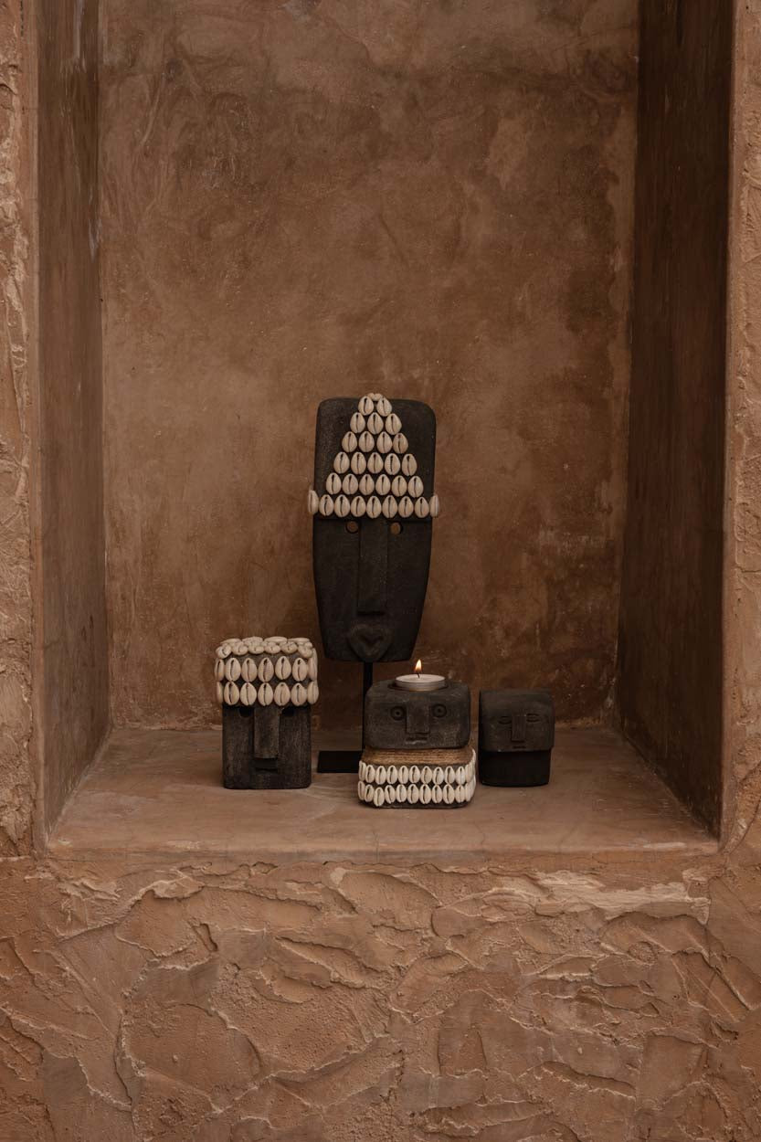 Kayu Living hand-carved grey sandstone Sumba statues decorated with cowrie shells displayed in a stone alcove.