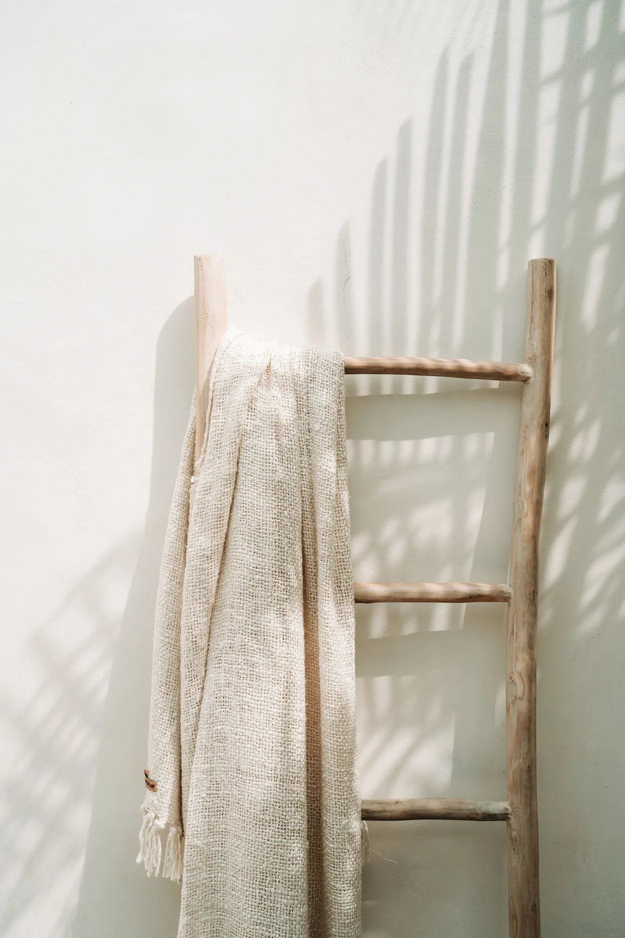 Kayu Living Tulum teak wood decorative ladder with a beige woven throw blanket against a white wall