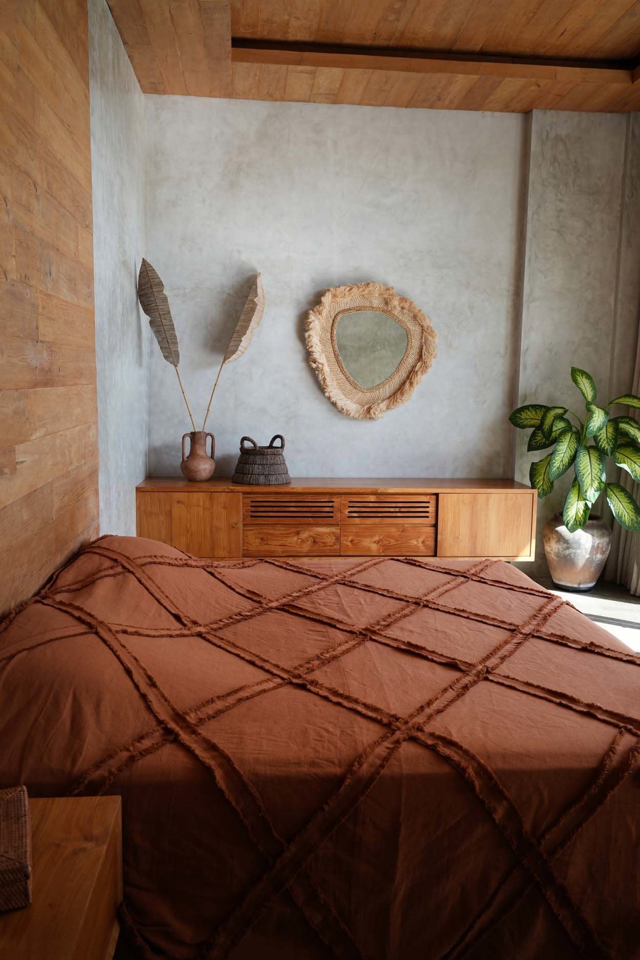 Kayu Living terracotta cotton bed throw with a textured plaid design draped over a bed in a rustic bedroom setting.