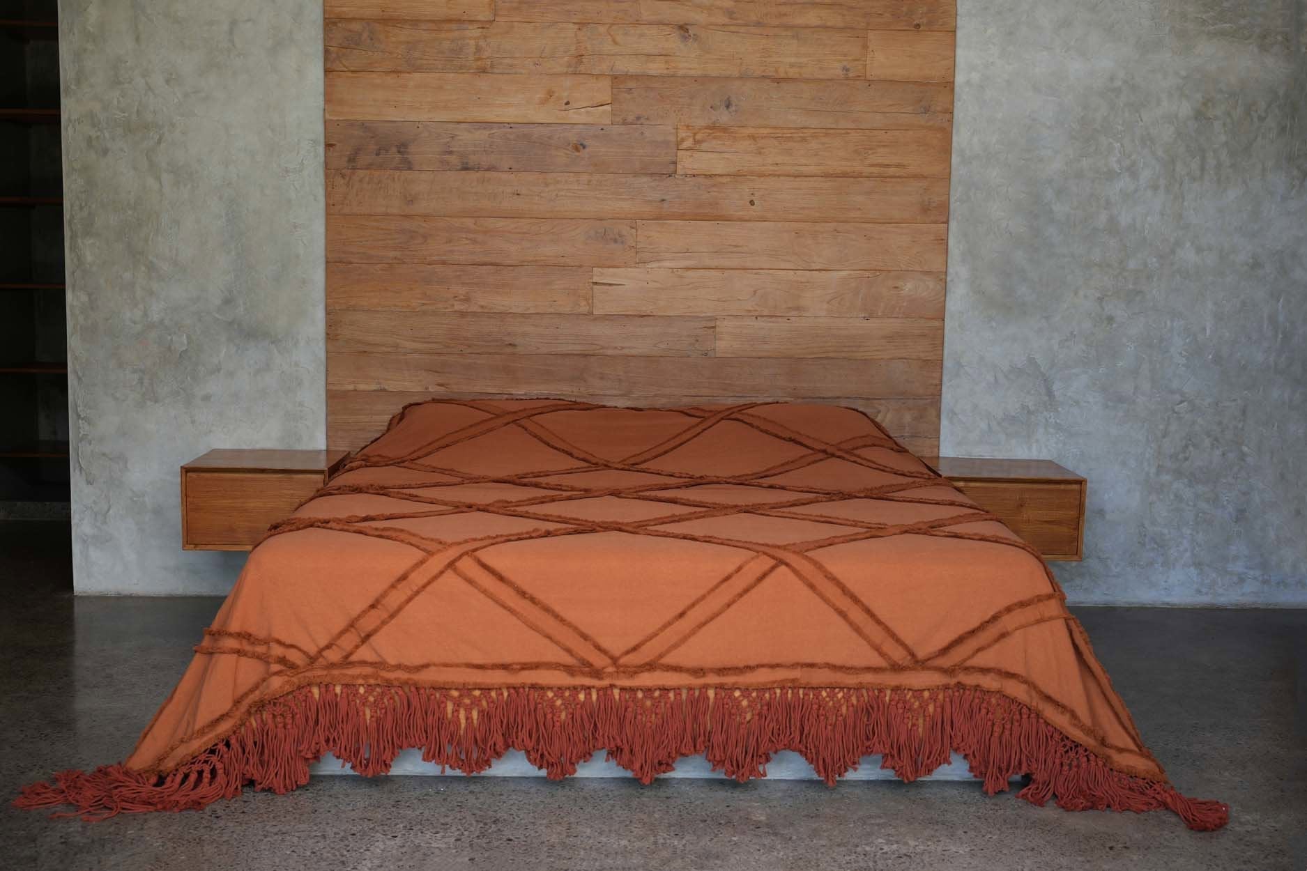 Kayu Living terracotta cotton bed throw with a diamond plaid pattern and decorative fringe draped over a bed.