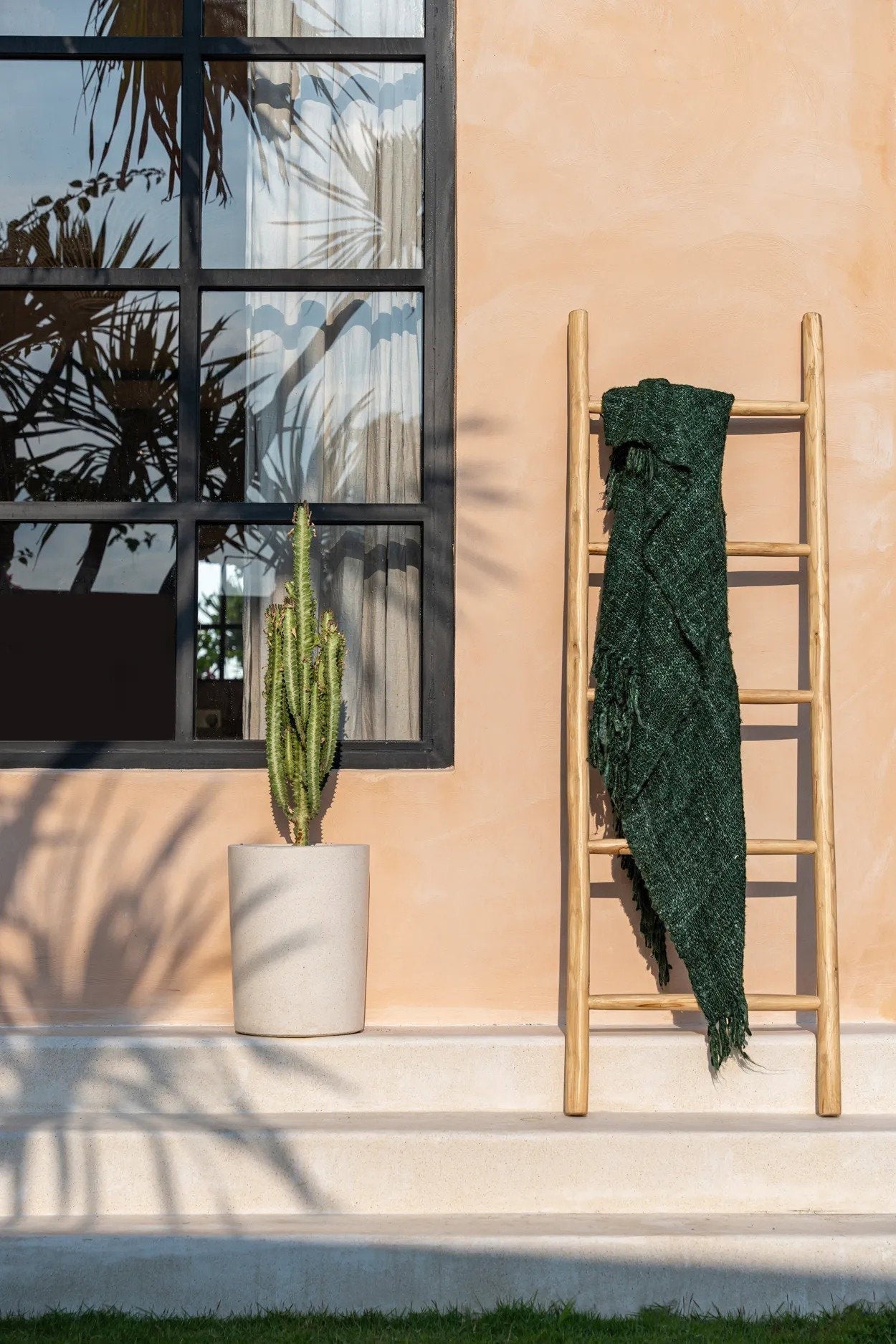 Kayu Living Tulum teak wood ladder leaning against a peach wall with a draped dark green throw blanket