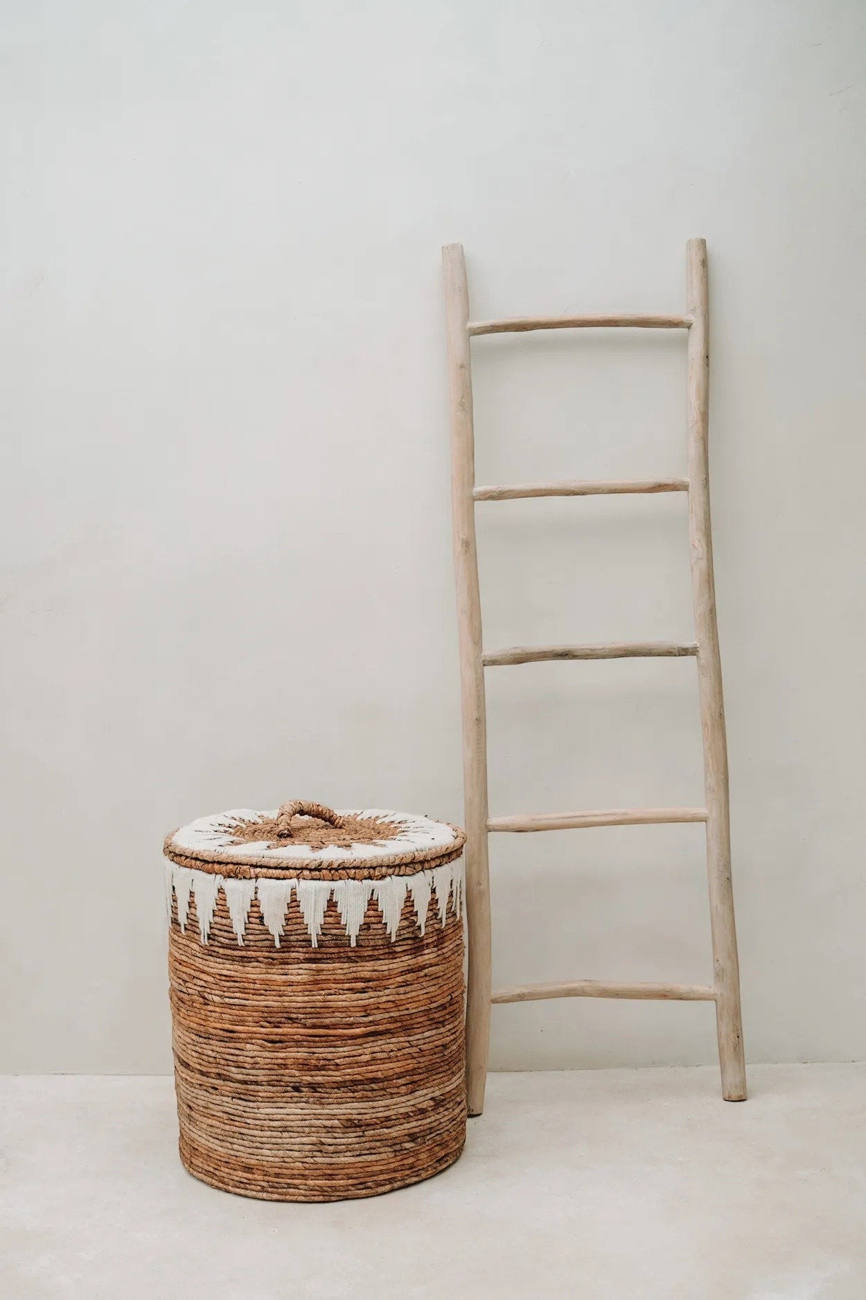 Kayu Living Tulum teak wood decorative ladder leaning against a wall next to a woven seagrass storage basket