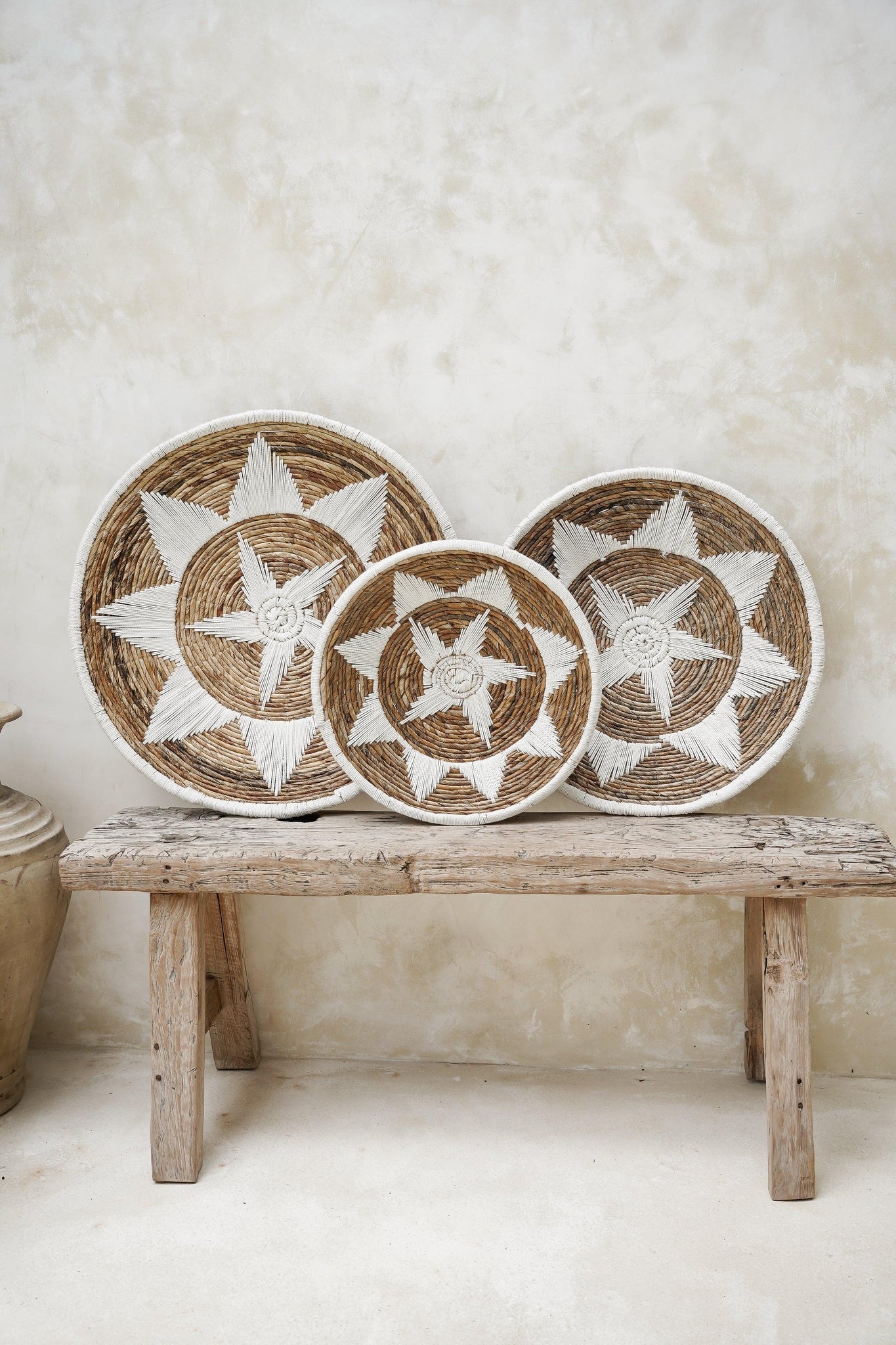 Kayu Living Uluwatu handmade brown and white banana leaf and cotton wall baskets in three sizes on a rustic bench