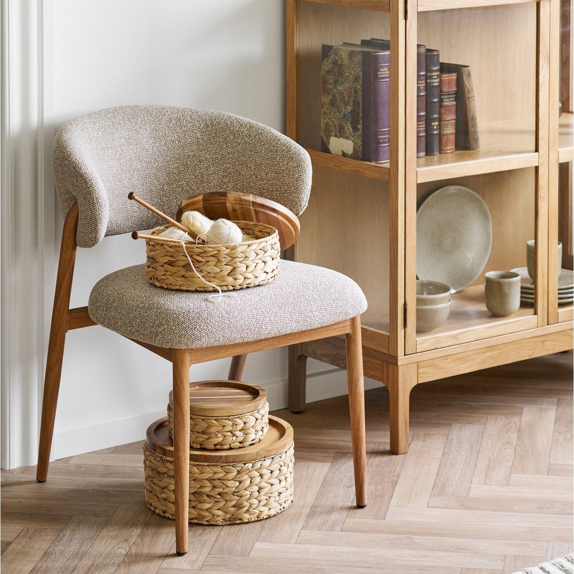 Kayu Living set of three natural water hyacinth baskets with wooden lids displayed on a modern upholstered chair.